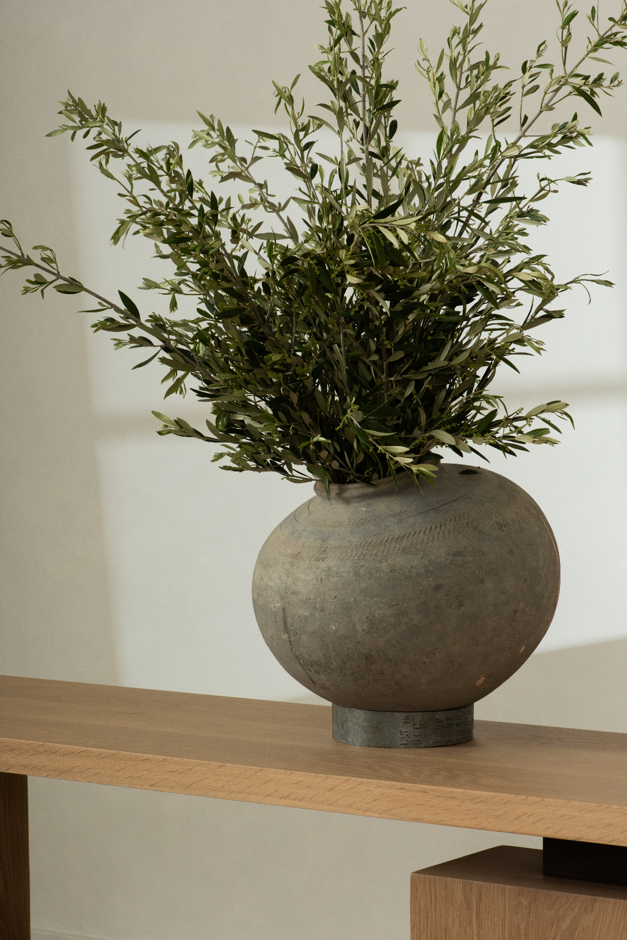 Olive branches in a stoneware vase on a wood console
